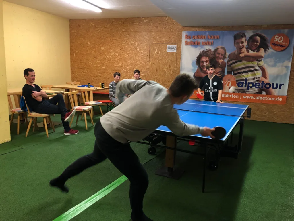 Jugendliche spielen Tischtennis, weitere sehen zu.